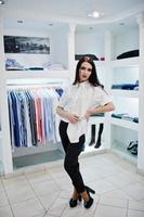 hermosa chica morena en la boutique de la tienda de ropa en ropa casual, blusa blanca y pantalones negros. foto