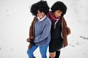 Two curly hair african american woman wear on sheepskin coat and gloves posed at winter day. photo