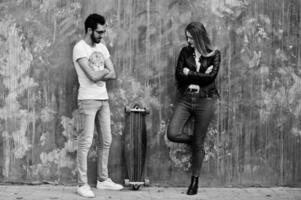 Cool multiracial couple posing against wall with longboard. photo