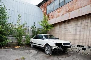 coche blanco desmontado sin faros, parachoques y motor en la antigua fábrica. foto