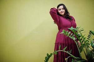 atractiva mujer del sur de Asia con un vestido de color rojo intenso posó en el estudio sobre un fondo verde con vegetación. foto