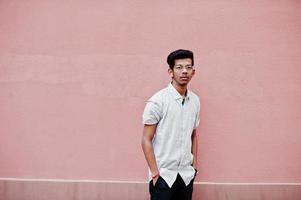 Young indian man on shirt and glasses posed against pink wall. photo