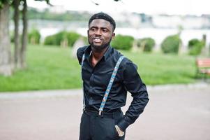 Young stylish african american man wear on all black with suspenders posed outdoor. photo