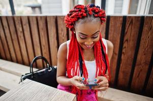 Fashionable african american girl at pink pants and red dreads posed outdoor with mobile phone. photo