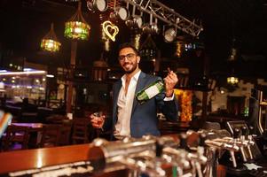 apuesto hombre árabe bien vestido con vaso de whisky y cigarro posado en el pub. foto