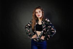 una guapa morena usa camisa militar y jeans, posando en el estudio con fondo gris. retrato de modelo de estudio. foto