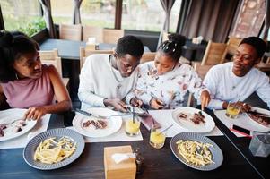 Happy african friends sitting, chatting in cafe and eat food. Group of black peoples meeting in restaurant and have dinner. Surprised face when seen guest check. photo