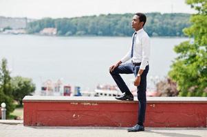 Stylish african american business man at pants and shirt posed outdoor against lake. photo