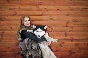 Red haired girl with husky dog against wooden wall. photo