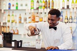camarero afroamericano en el bar con agitador. preparación de bebidas alcohólicas. foto