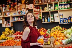 Girl in red holding different vegetables on fruits store. photo