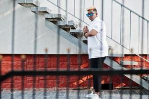 Stylish arabian muslim boy with originally hair and sunglasses posed on streets at ladder. photo