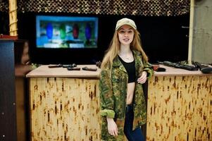 Military girl in camouflage uniform against army background on shooting range. photo