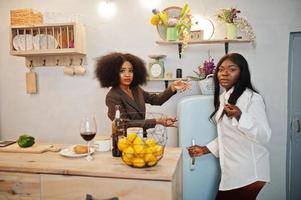 Two african american female friends women spending time at kitchen with wine. Black girlfriends  relaxing at home and eat chocolate. photo