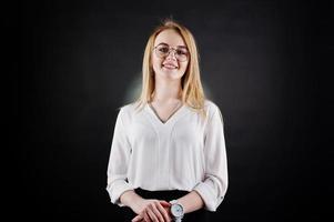 Studio portrait of blonde businesswoman in glasses, white blouse and black skirt against dark background. Successful woman and stylish girl concept. photo