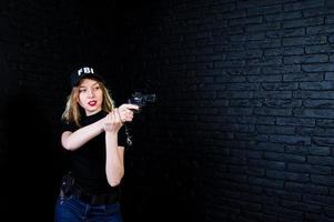 FBI female agent in cap and with gun at studio against dark brick wall. photo