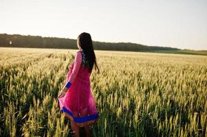 tierna niña india en sari, con maquillaje de labios violetas posada en el campo al atardecer. modelo indio de moda. foto