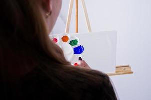 Beautiful woman artist painter with brushes and oil canvas posing in studio isolated on white. photo