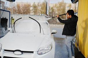 hombre del sur de asia o hombre indio lavando su transporte blanco en el lavado de autos. foto