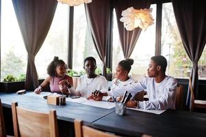 Happy african friends sitting and chatting in cafe. Group of black peoples meeting in restaurant and hold hands together. photo