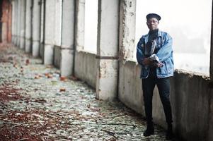 African american man in jeans jacket, beret and eyeglasses at abandoned brick factory. photo