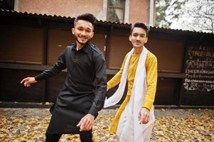 Two indian stylish mans friends in traditional clothes dancing outdoor. Navaratri dance. photo