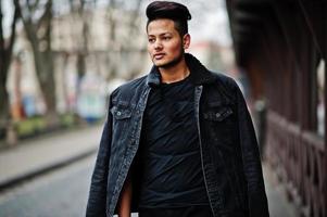 hombre indio guapo y de moda con chaqueta negra de jeans posada al aire libre. foto