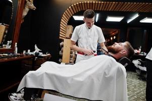 un joven barbudo que se corta el pelo con un peluquero mientras se sienta en una silla en la barbería. alma de barbero. foto