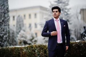 elegante modelo de hombre macho indio con traje y corbata rosa posado en el día de invierno. foto