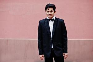 Young indian man on suit and bow tie posed against pink wall. photo