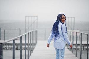 Stylish african american girl with dreads holding mobile phone at hand, outdoor on pier against frozen lake at snowy weather. photo