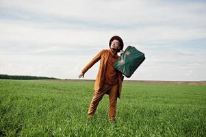 hombre elegante con gafas, chaqueta marrón y sombrero con bolso posado en campo verde. foto