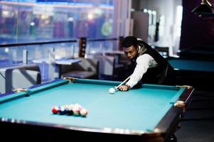 Young handsome african man wearing white shirt, black vest and bow tie play pool billiard. photo