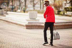 parte posterior del modelo de hombre afroamericano de moda en traje rojo, con cabello destacado y bolso posado en la calle. foto