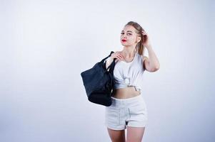 Amazing fit sexy body brunette caucasian girl posing at studio against white background on shorts and top with black sport bag. photo