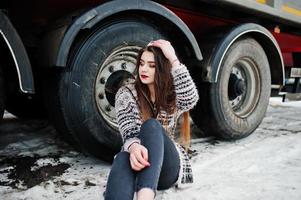 Brunette stylish casual girl in cap sitting against truck wheels. photo