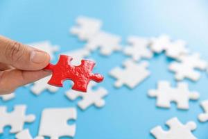 Hand putting piece of red jigsaw puzzle on blue background. Team business success partnership or teamwork. photo