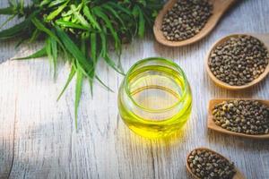 Hemp seeds in wooden spoon and hemp oil in a glass jar on brown wooden table. medical marijuana concept, CBD cannabis OIL. photo