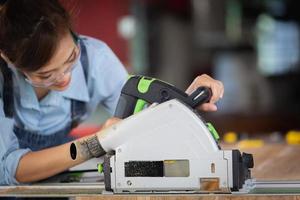 A female carpenter uses a chainsaw while working in a wood shop. photo