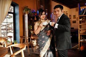 Elegant and fashionable indian friends couple of woman in saree and man in suit sitting on cafe and drinking tea. photo