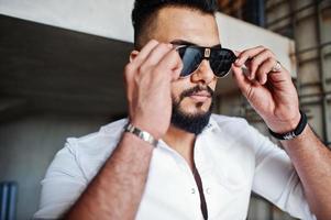 Close up photo of stylish arabian man model in white shirt and sunglasses. Beard attractive arab guy.