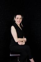 Portrait of a beautiful brunette girl in black jumpsuit sitting and posing in the studio. photo