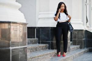 elegante mujer de negocios afroamericana en las calles de la ciudad hablando por teléfono móvil. foto