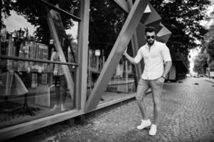 Elegante modelo de hombre árabe alto con camisa blanca, jeans y gafas de sol en la calle de la ciudad. barba chico árabe atractivo. foto