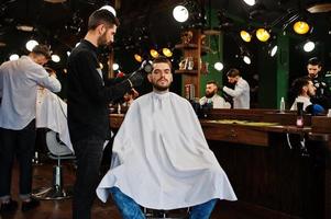 Handsome bearded man at the barbershop, barber at work, using hair dryer. photo