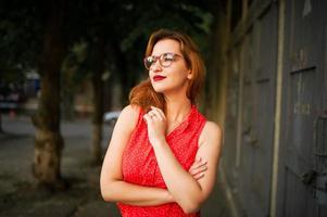 Attractive redhaired woman in eyeglasses, wear on red blouse and jeans skirt posing. photo