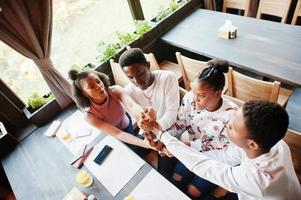 Happy african friends sitting and chatting in cafe. Group of black peoples meeting and play games by hands in restaurant. photo