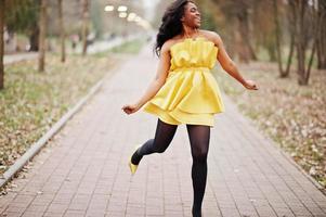 Stylish african american woman at yellow dress posed against autumn park and jumping. photo