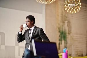 Business african american man wear on black suit and glasses at office, drinking morning coffee before work day. photo