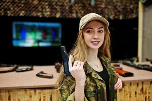 Military girl in camouflage uniform with gun at hand against army background on shooting range. photo